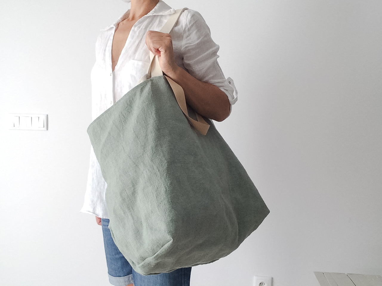 women in white linen shirt and jeans wears a green linen beach bag